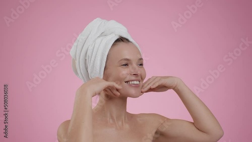 Facebuilding concept. Semi profile portrait of middle aged woman with towel on head doing face massage after shower photo