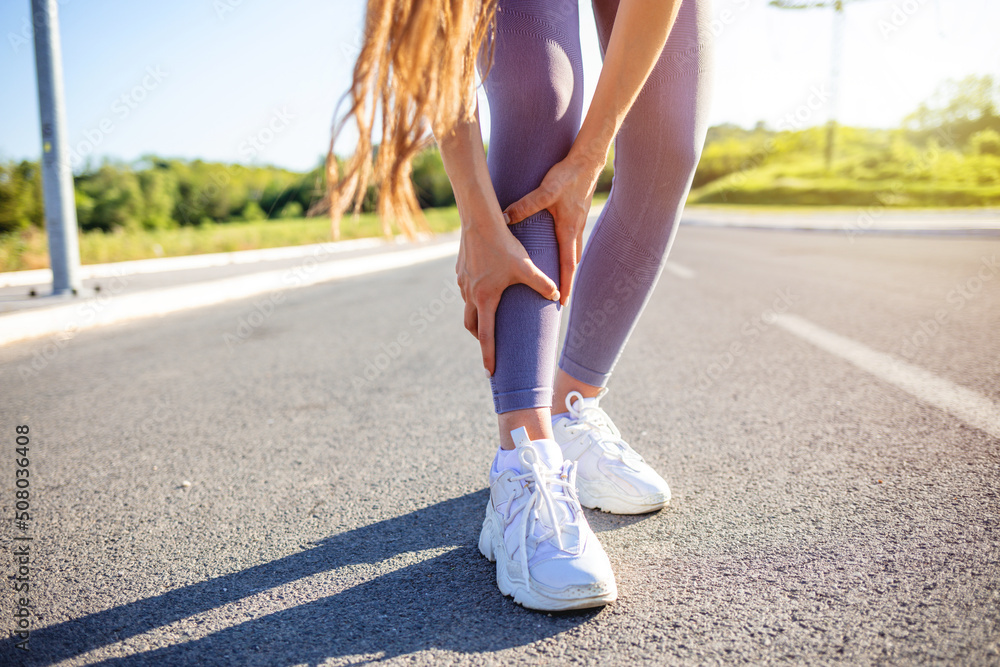 Female athlete runner muscle and ankle injury after jogging. Woman runner touching muscle in painful. Muscle and ankle injury concept. Woman suffering from a leg injury. Healthy lifestyle concept.