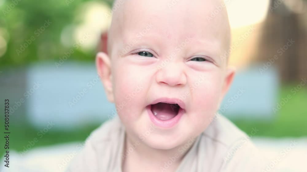 close-up portrait funny face infant baby lying on green grass outdoor sunny day. caucasian blue eyed child kid looking camera making cute sweet grimace. baby opening mouth showing first white teeth close-up portrait funny face infant baby lying on green grass outdoor sunny day. caucasian blue eyed child kid looking camera making cute sweet grimace. baby opening mouth showing first white teeth