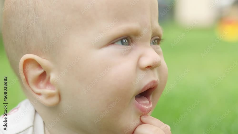 happy infant baby lying green meadow field touching grass trying eat, opening mouth, licking fingers and blades of grass. blue eyed caucasian baby portrait looking camera, making funny face, smiling happy infant baby lying green meadow field touching grass trying eat, opening mouth, licking fingers and blades of grass. blue eyed caucasian baby portrait looking camera, making funny face, smiling