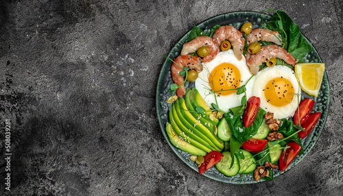 shrimps, prawns, soft fried egg, fresh salad, tomatoes, cucumbers and avocado on a dark background. Ketogenic diet breakfast. Keto, paleo lunch. Long banner format. top view