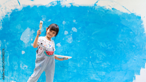 Adorable 5 years old asian little girl is smiling while painting the wall with water color at home, concept of art education for kid, homeschooling and learning activity by playing for child.