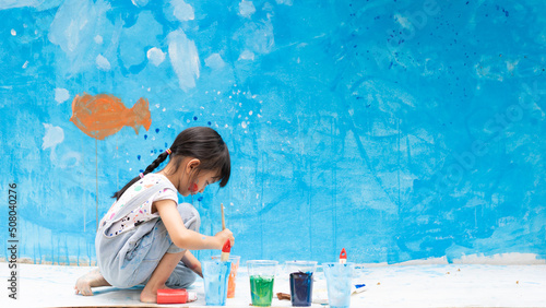 Adorable 5 years old asian little girl is smiling while painting the wall with water color at home, concept of art education for kid, homeschooling and learning activity by playing for child. photo