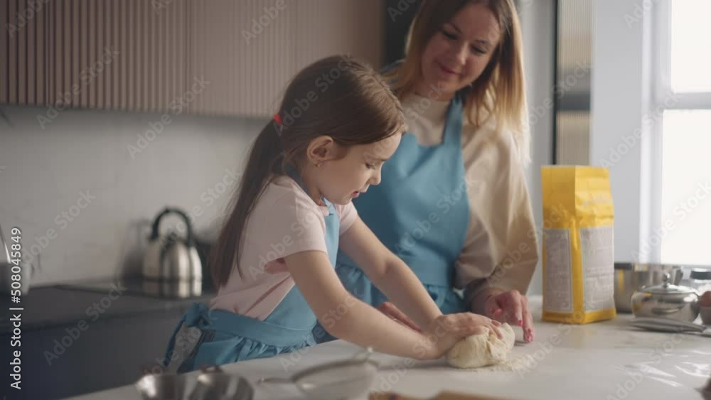 curious little girl is helping mother to cook in kitchen, learning to knead dough on table, cooking pie curious little girl is helping mother to cook in kitchen, learning to knead dough on table, cooking pie