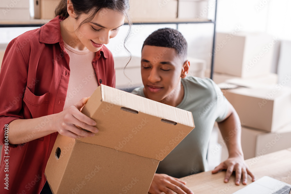 Smiling multiethnic sellers looking at open carton box in online web store. Smiling multiethnic sellers looking at open carton box in online web store.