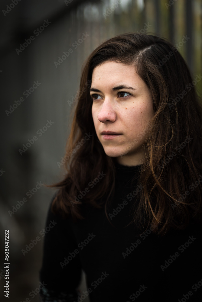 Portrait of a 27 year old white woman, dressed in black, standing against a metal fence Portrait of a 27 year old white woman, dressed in black, standing against a metal fence