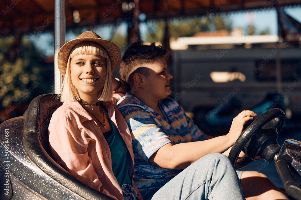 Smiling woman and her girlfriend driving bumper car at amusement park.
