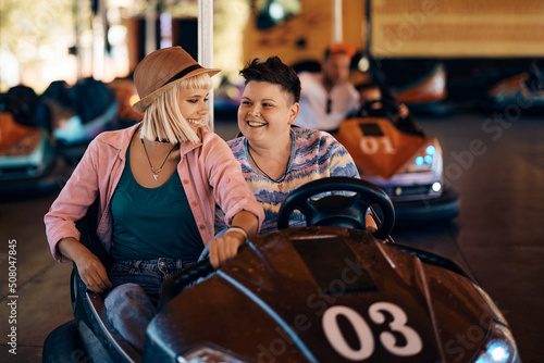 Young lesbian couple enjoys while driving bumper car at amusement park.