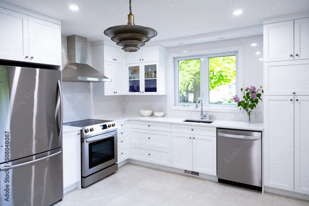 Selective focus view of large modern kitchen with white cabinets, counter and backsplash, as well as stainless steel appliances Selective focus view of large modern kitchen with white cabinets, counter and backsplash, as well as stainless steel appliances