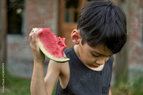 argentine child holding a slice of watermelon with one hand and looking down at the mess he is making with the juice. Selective focus