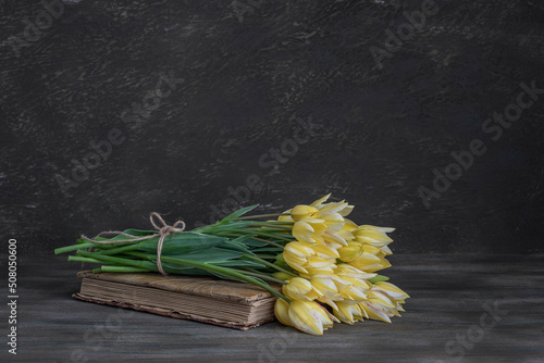 Still life. Tulips Bouquet and an old book on a wooden table. Rustic style.
