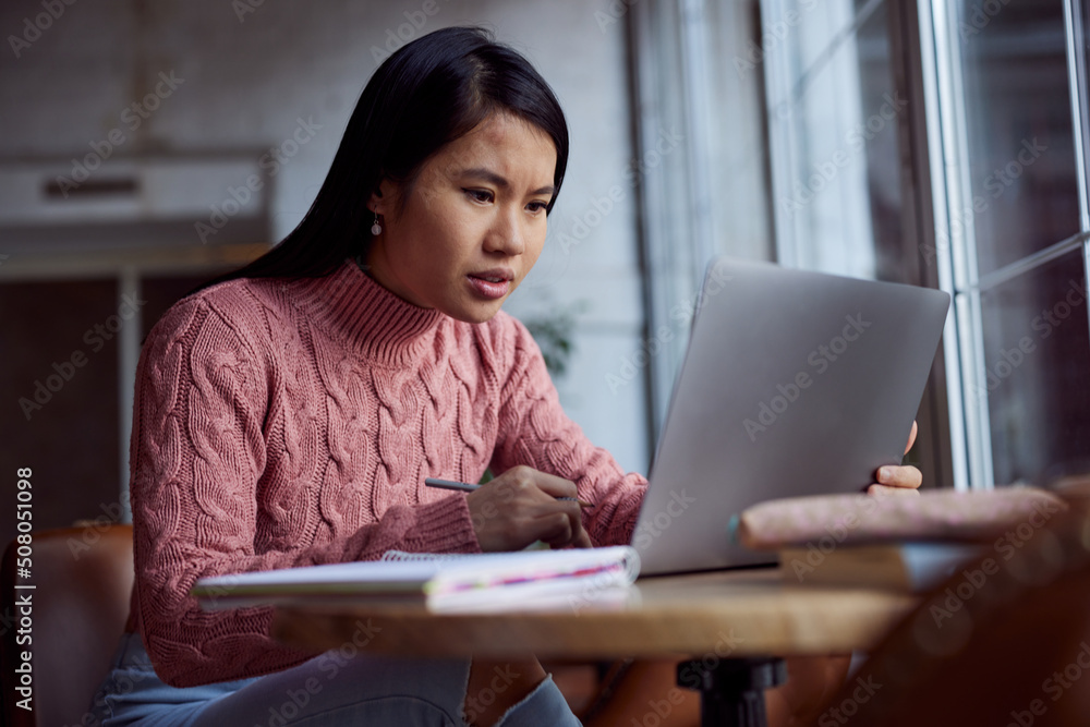 An Asian girl follows online lectures on the laptop at a cafe. An Asian girl follows online lectures on the laptop at a cafe.