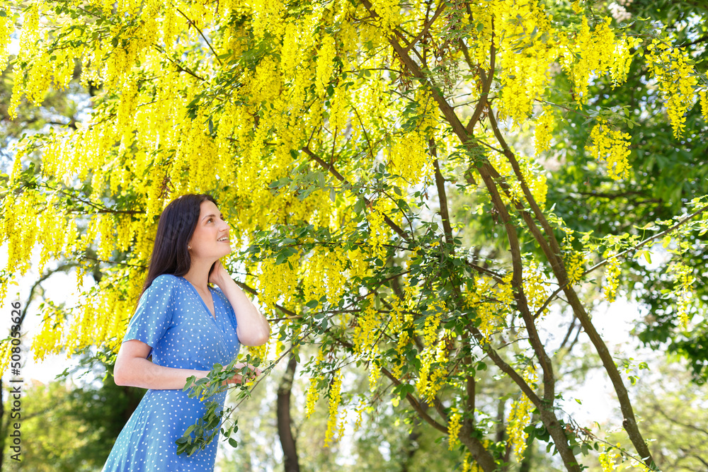 a woman in a blue dress near a blooming yellow tree on a walk in the summer