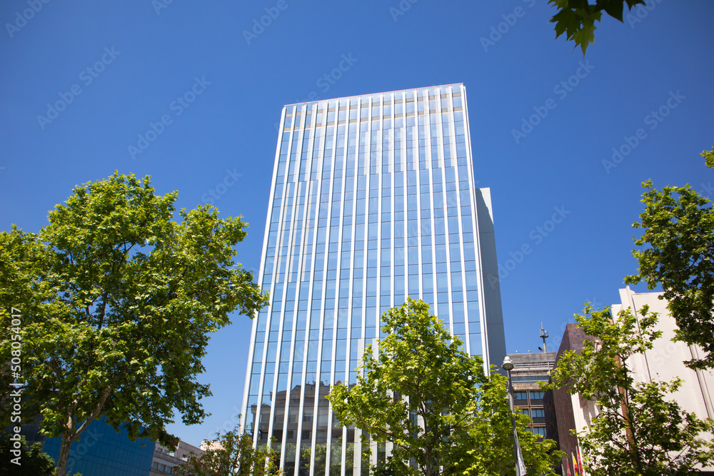 Modern tall multistory building glass facade against blue sky in summer city. Residential or office building, facilities. Construction business. Real estate investment. Cityscape view. Urban scene.