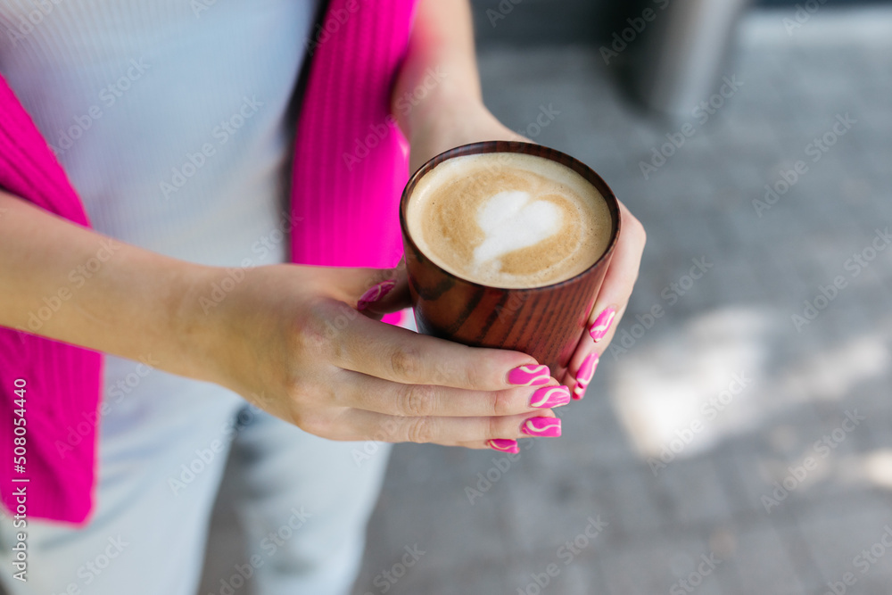 The girl drinks coffee. Girl holding coffee in her hands. Delicious cappuccino in the hands of a girl. Coffee and cappuccino in hand. Good morning. Delicious coffee.