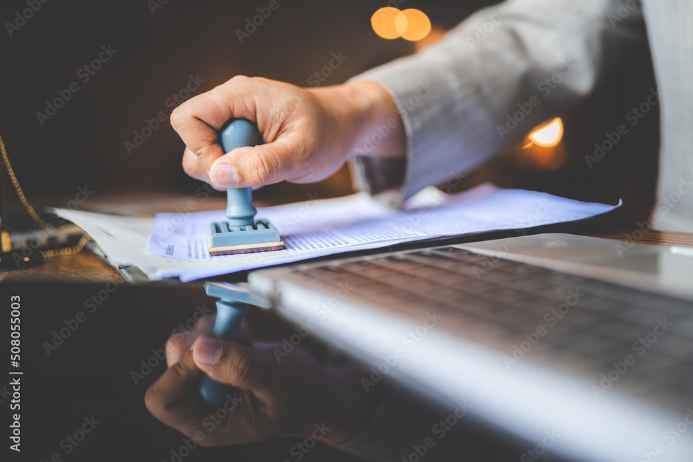 Close-up of a person's hand stamping with passed and approved stamp on certificate document public paper at desk, notary or business people work from home, isolated for coronavirus COVID-19 protection - obrazy, fototapety, plakaty 