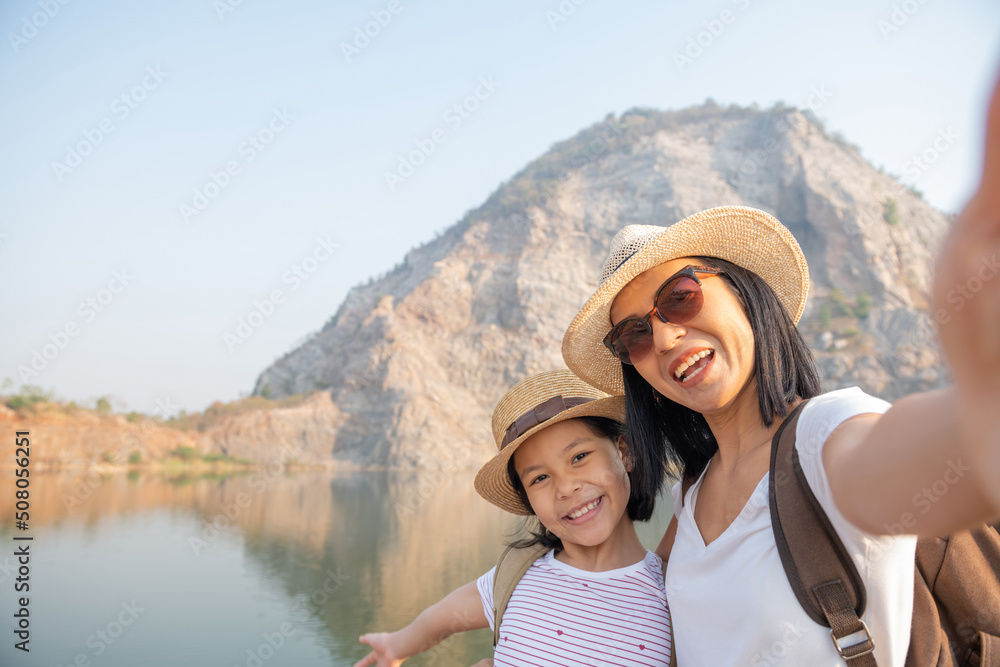 Happy family standing near the lake at the day time, happy asian family taking selfie hiking adventure. Happiness mother and daughter at sunny day under sunlight. Summer vacations concept.