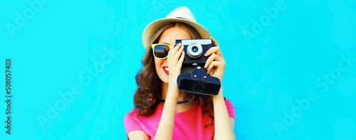 Summer portrait of young woman photographer with film camera on blue background