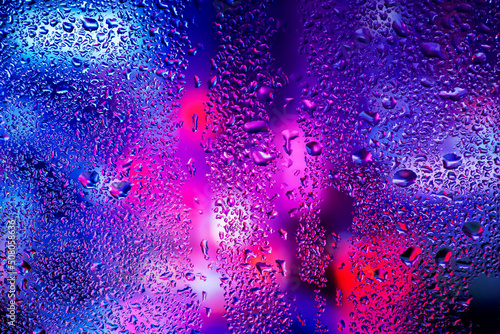 Rain drops and condensation on the window glass against the background of the neon light