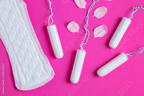 Female tampons with with cherry petals and woman gasket on a pink background. Hygienic white tampon for women.