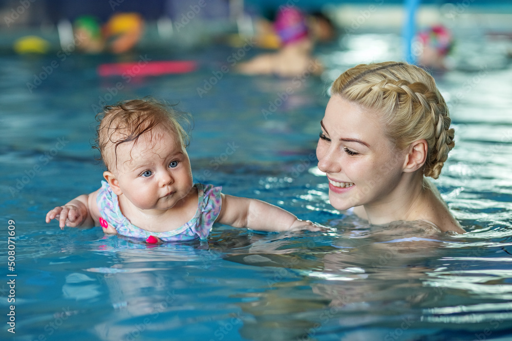 Young beautiful blonde mother with baby in pool. Concept of sport, training and family