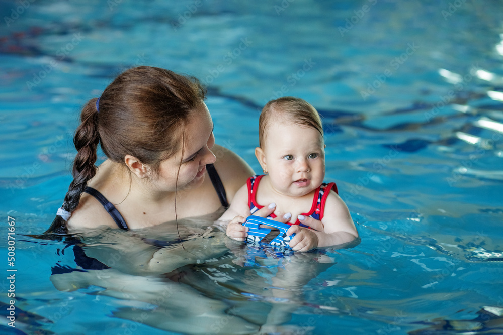 Smiling happy mother with baby girl in swimming pool. Sport, training and family concept