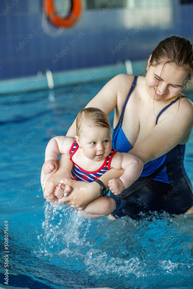 Smiling happy mother with baby girl in swimming pool. Sport, training and family concept