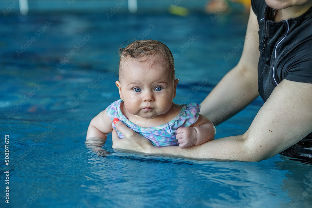 Mom supports baby with hands in swimming pool, teaches to swim and dive. Mom supports baby with hands in swimming pool, teaches to swim and dive.