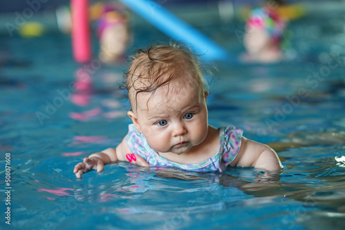 Mom supports baby with hands in swimming pool, teaches to swim and dive.