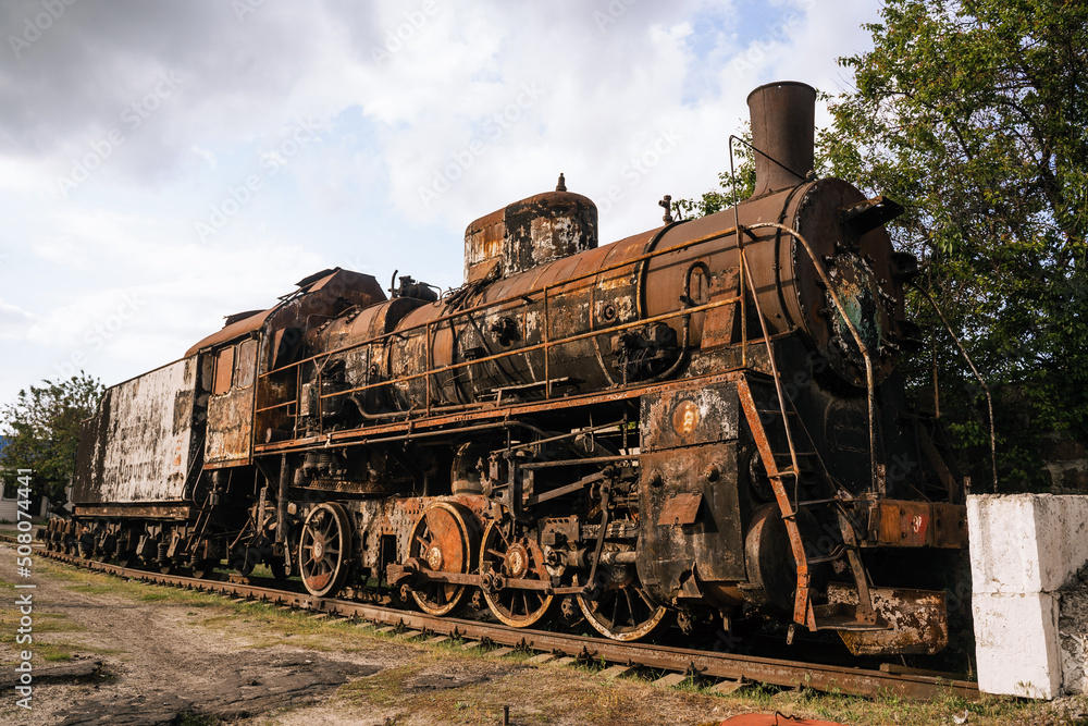 Naklejka premium Burned-out locomotive is a museum exhibit at the railway station in the city of Trostyanets. Sumy region. Civil buildings. Russian military invasion of Ukraine.