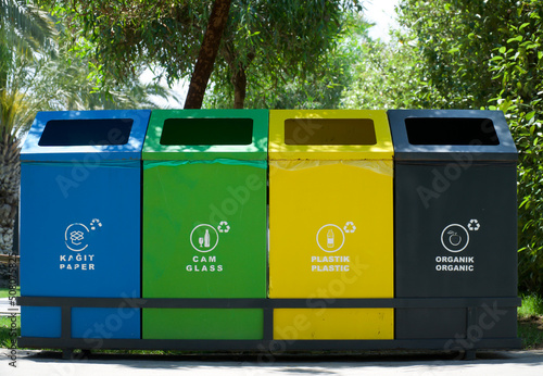 Different colored trash cans with inscriptions paper, plastic, glass and organic waste suitable for recycling. Segregate waste, sorting garbage, waste management. Nature green background