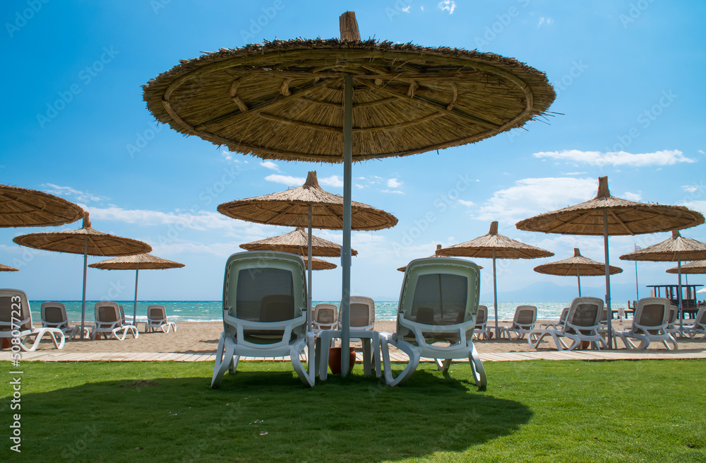  Beach umbrellas and deck chairs at sunny day.  Straw umbrellas in front of the sea, summer time