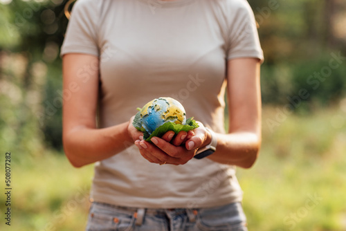 Young woman holding small planet in hands against spring or summer green background. Ecology, environment and Earth day concept. Elements of this image furnished by NASA.