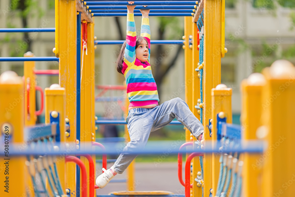 a little girl hangs on a childrens ladder on a bright playground in the park in summer