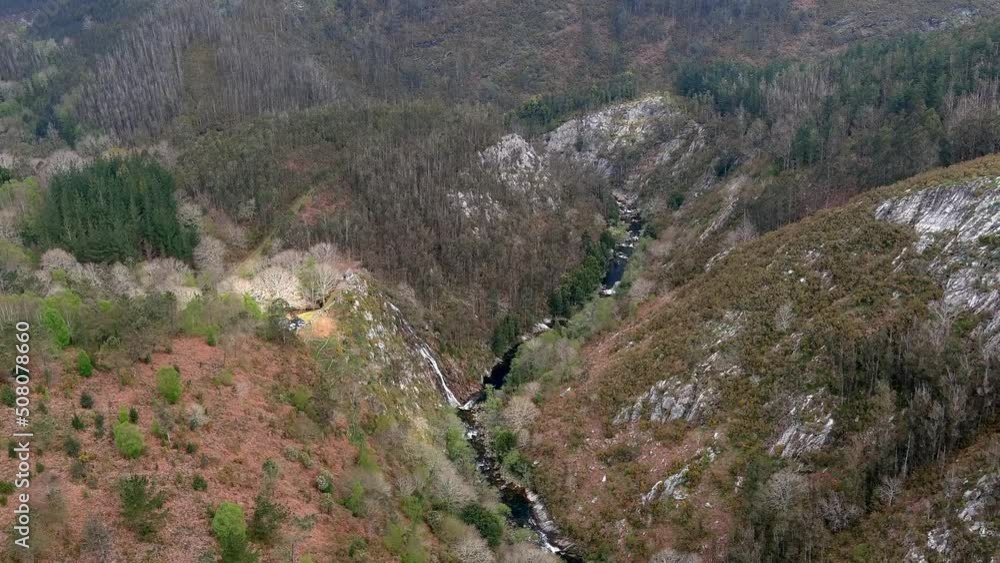 hills with eucalyptus trees and the valley of the River Sor with the waterfall on the cliff of the slope slope of the valley. Drone shot, traveling side to right. Mirador Aguas Caidas, Galicia, Spain hills with eucalyptus trees and the valley of the River Sor with the waterfall on the cliff of the slope slope of the valley. Drone shot, traveling side to right. Mirador Aguas Caidas, Galicia, Spain