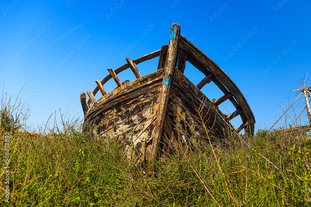 the alone wreck of a dilapidated boat on land covered with grass the alone wreck of a dilapidated boat on land covered with grass