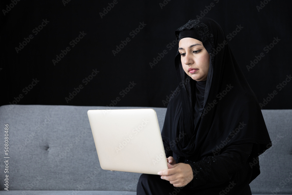muslim woman using laptop computer on sofa and black background muslim woman using laptop computer on sofa and black background