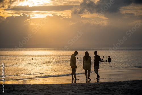 silhouette of of trio of people standing around enjoying during sunset dusk at radhasagar beach with the waves coming on the shore in havelock andaman
