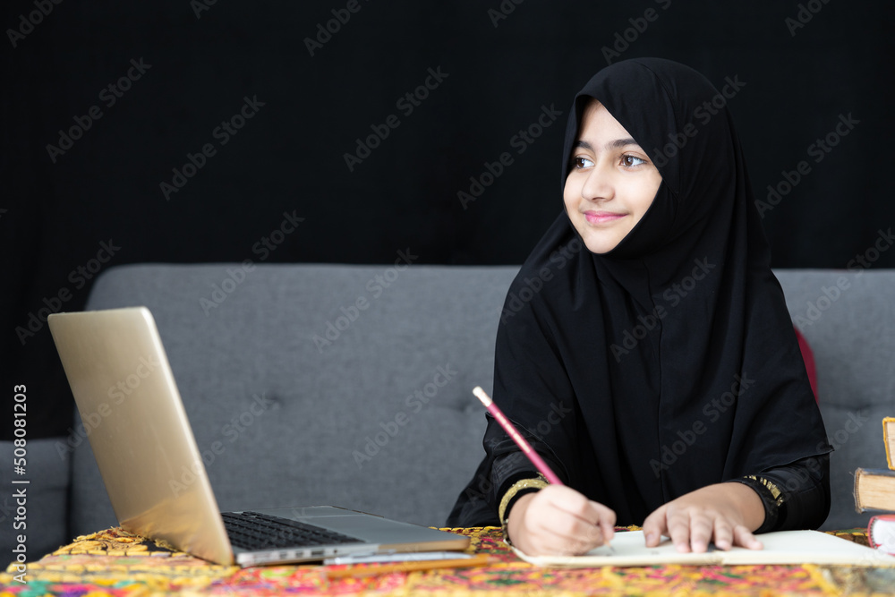 muslim girl writing on notebook, using a laptop computer and online learning at home muslim girl writing on notebook, using a laptop computer and online learning at home