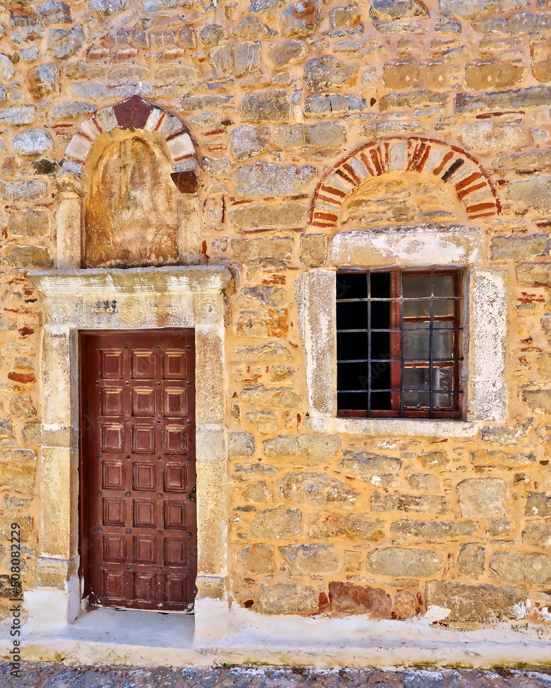 An old stone house front with a brown wooden door and a window. Pyrgi, Chios island, Greece.