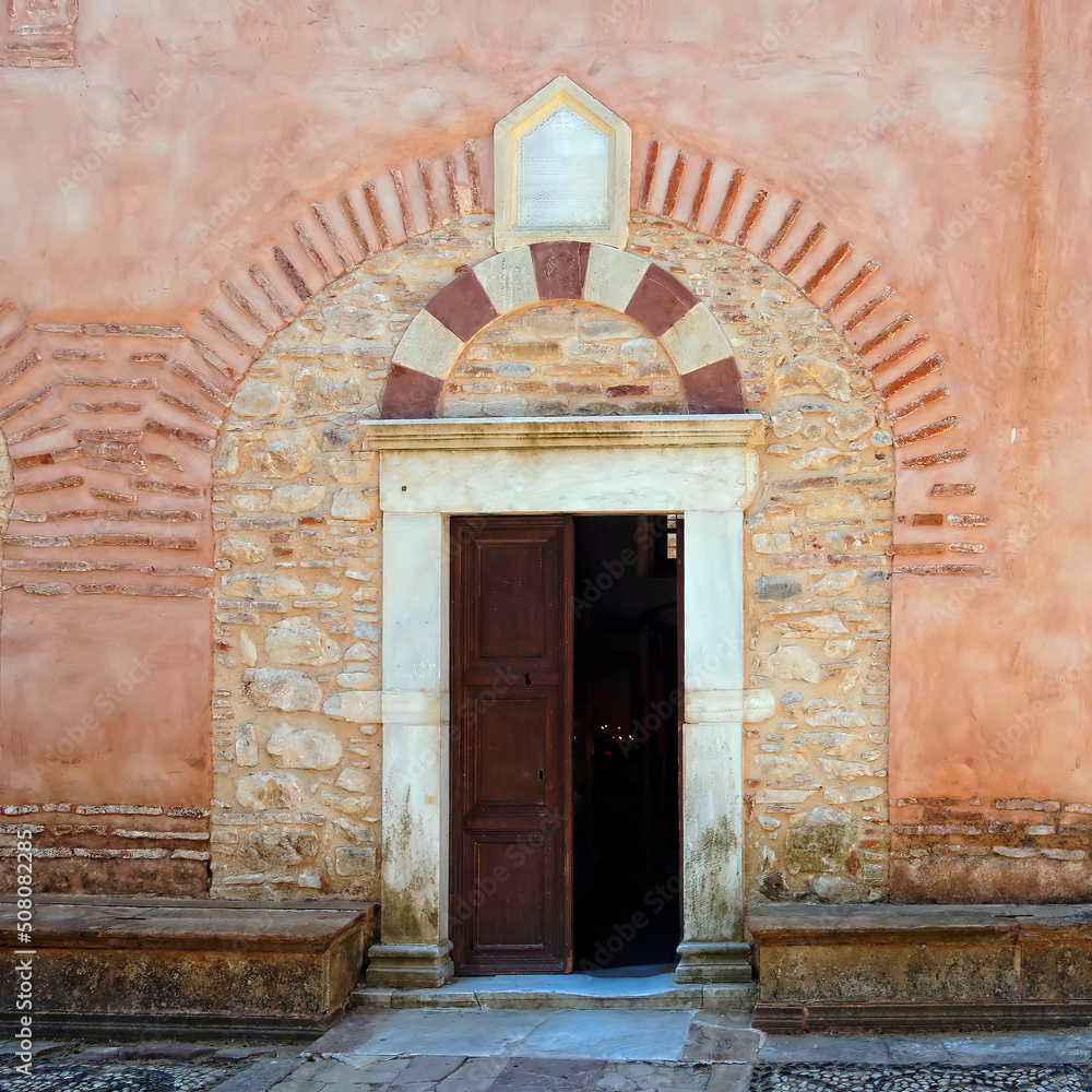 An old medieval church entrance with an open wooden door and a decorative arch. Chios island, Greece. An old medieval church entrance with an open wooden door and a decorative arch. Chios island, Greece.