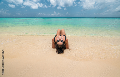 young hispanic woman lying on sand looking back wearing sunglasses