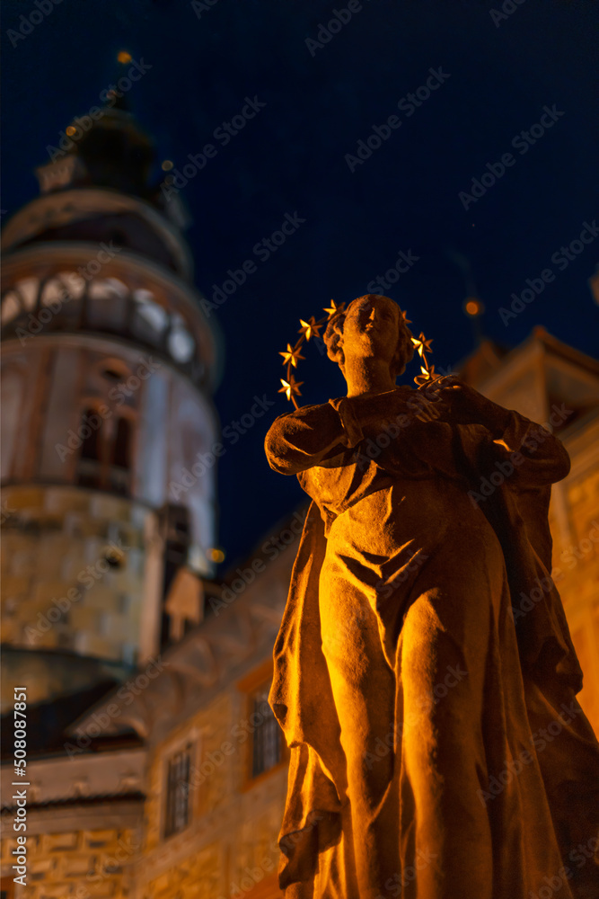 Statue of the saint with the tower of the Cesky Krumlov castle in the background. Night photo. Cesky Krumlov, South Bohemia, Czech Republic.