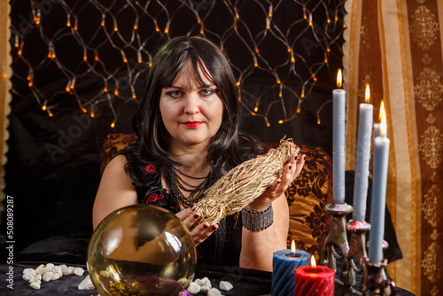 Fortune teller brunette woman in a magical salon is engaged in magic with herbs.