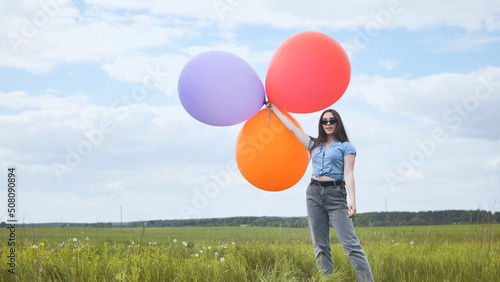 Happy girl with big multicolored balloons posing on the field.