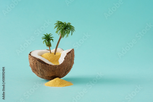 Creative layout made of coconut, color sand and palm trees on blue background. Tropical beach concept with copy space. Minimal summer idea. photo