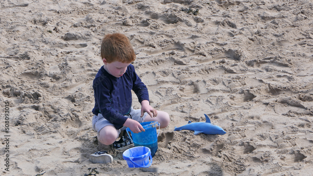 Red headed boy playing on a sandy beach in Northern Ireland Holidays UK Red headed boy playing on a sandy beach in Northern Ireland Holidays UK