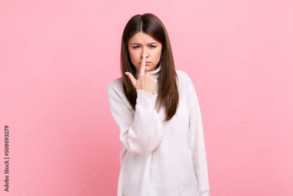 Pretty girl pointing finger at nose, showing lie gesture, blaming and suspicion you, body language, wearing white casual style sweater. Indoor studio shot isolated on pink background. Pretty girl pointing finger at nose, showing lie gesture, blaming and suspicion you, body language, wearing white casual style sweater. Indoor studio shot isolated on pink background.