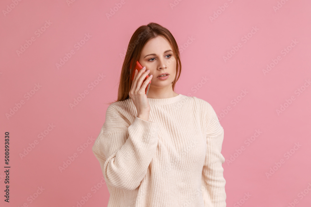 Portrait of winsome serious blond woman talking on smart phone, having bossy expression, looking away, conversation, wearing white sweater. Indoor studio shot isolated on pink background. Portrait of winsome serious blond woman talking on smart phone, having bossy expression, looking away, conversation, wearing white sweater. Indoor studio shot isolated on pink background.