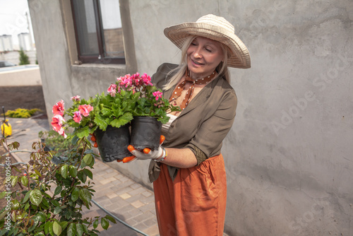 senior female gardener 60 years old  in abandoned backyard. Blond serene woman working planting flowers in garden at summer time. Gardening, hobby, leisure concept.